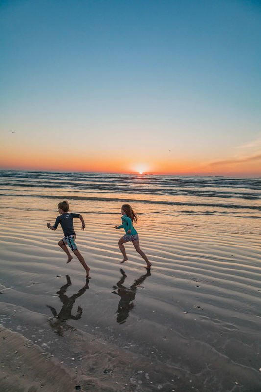 Children running along a beach at sunset